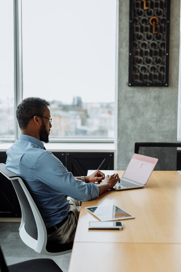 Black man working on laptop in modern office with city view, focused on technology and productivity.